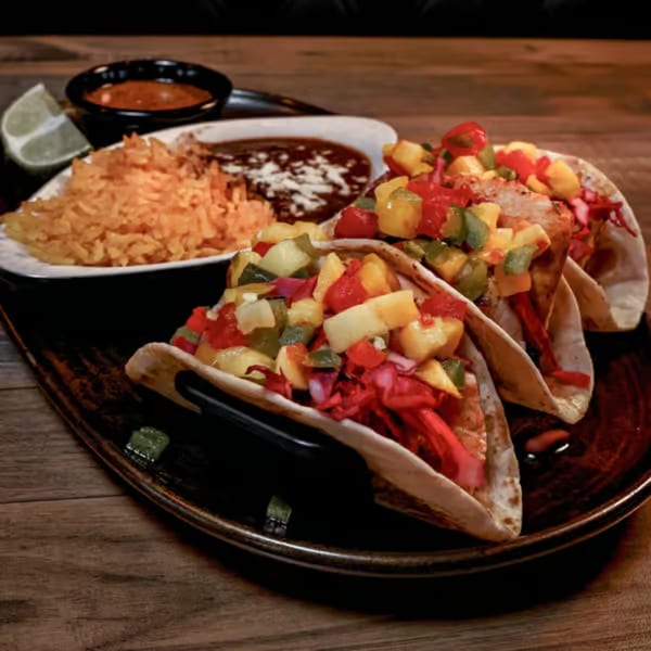 Three Santo Tequila tacos with colorful toppings, rice, and beans on a dark plate.