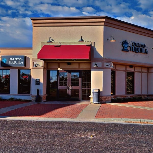 Exterior of Santo Tequila restaurant with a red awning, brick walkway, and blue sky.